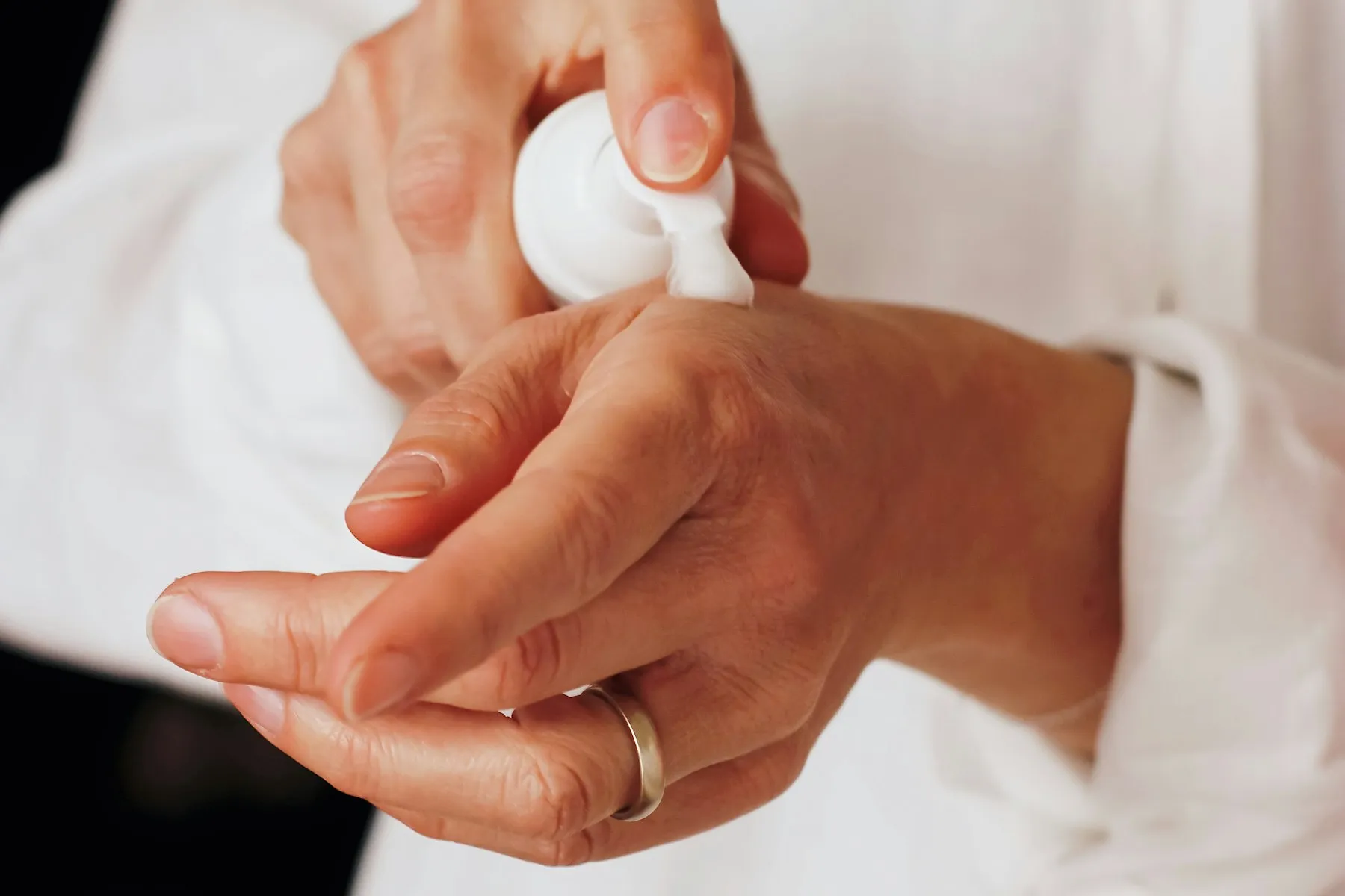 Hands smoothing lotion dispensed from a white pump bottle