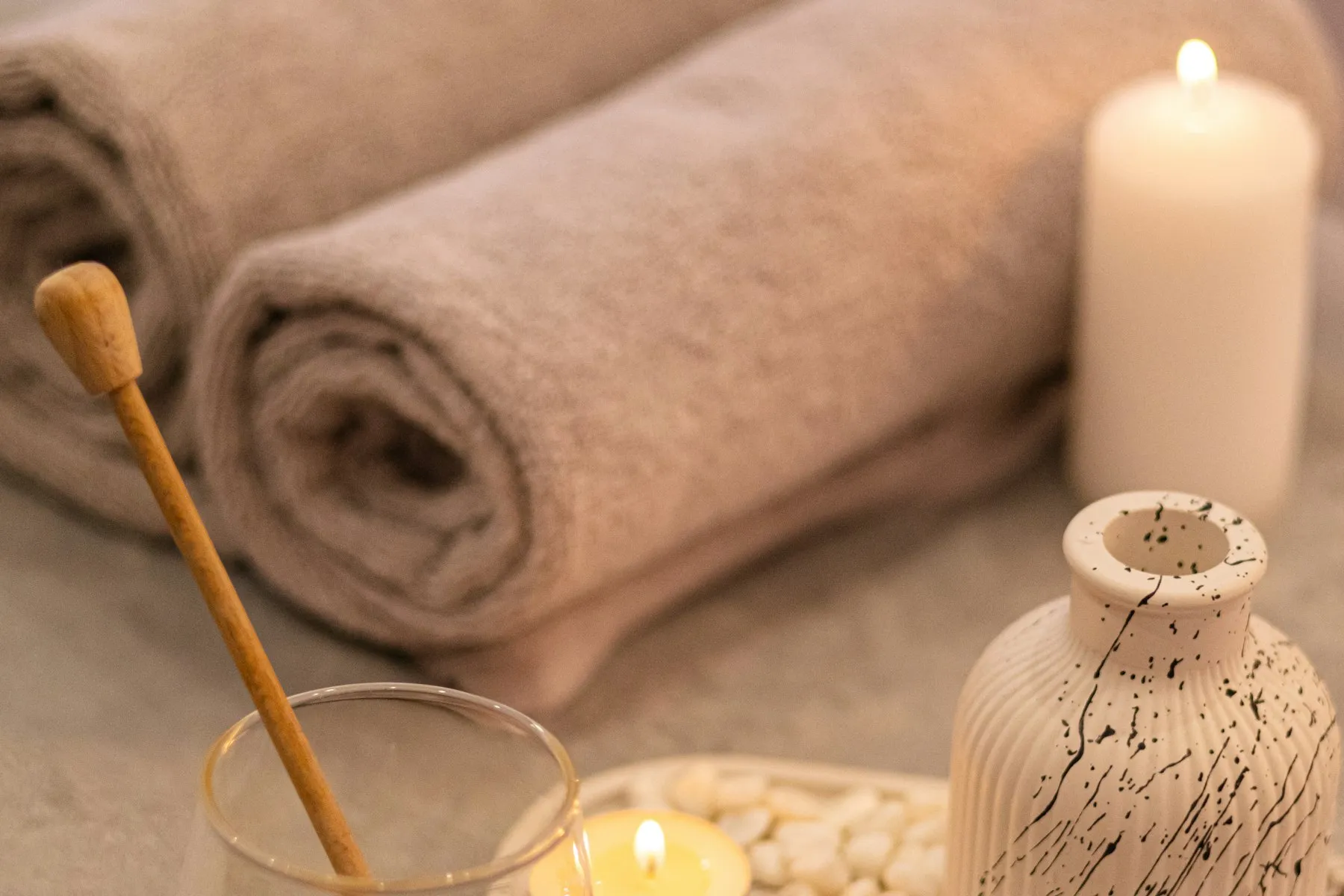 A spa table with lit candles, a diffuser and a small jar of honey
