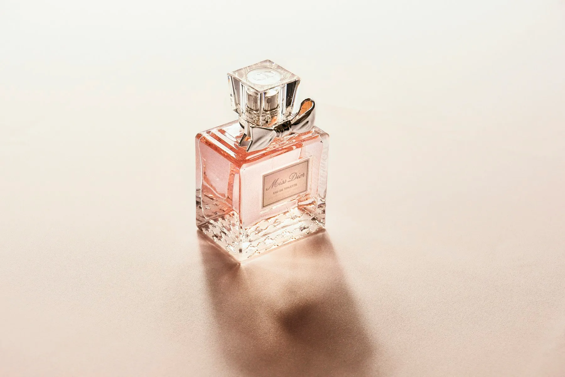 A softly lit pink glass perfume bottle with a ribbon at its neck
