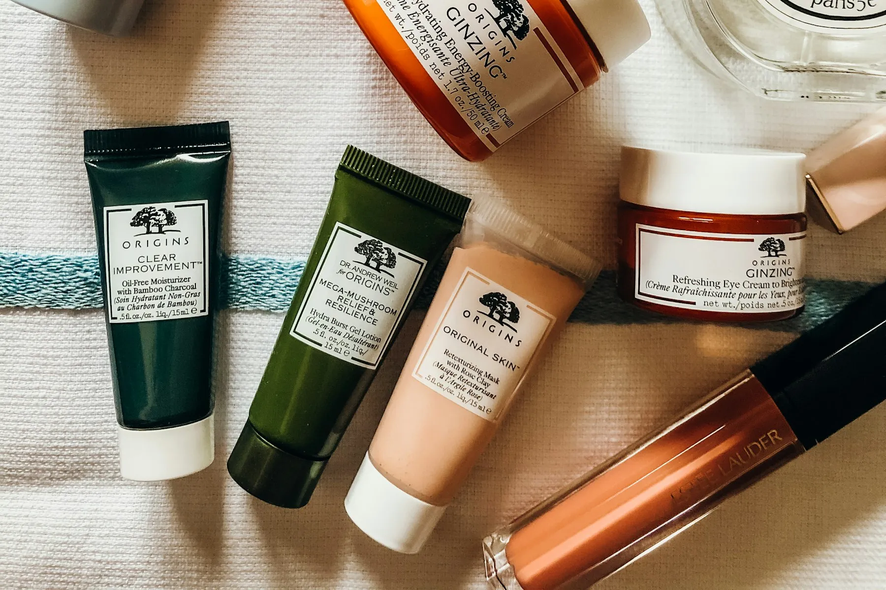 Skincare bottles and a green jade roller laid out on a striped towel