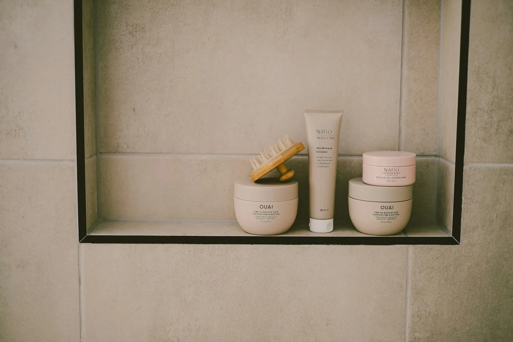Cosmetic bottles and jars arranged neatly in a tiled bathroom niche