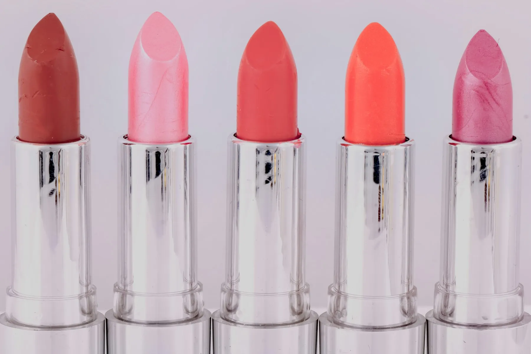 Five lipstick bullets in a row, ranging from pale pink to coral