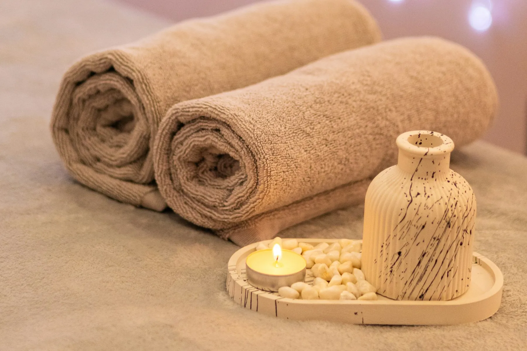 Rolled beige towels and a wooden diffuser arranged beside a lit candle