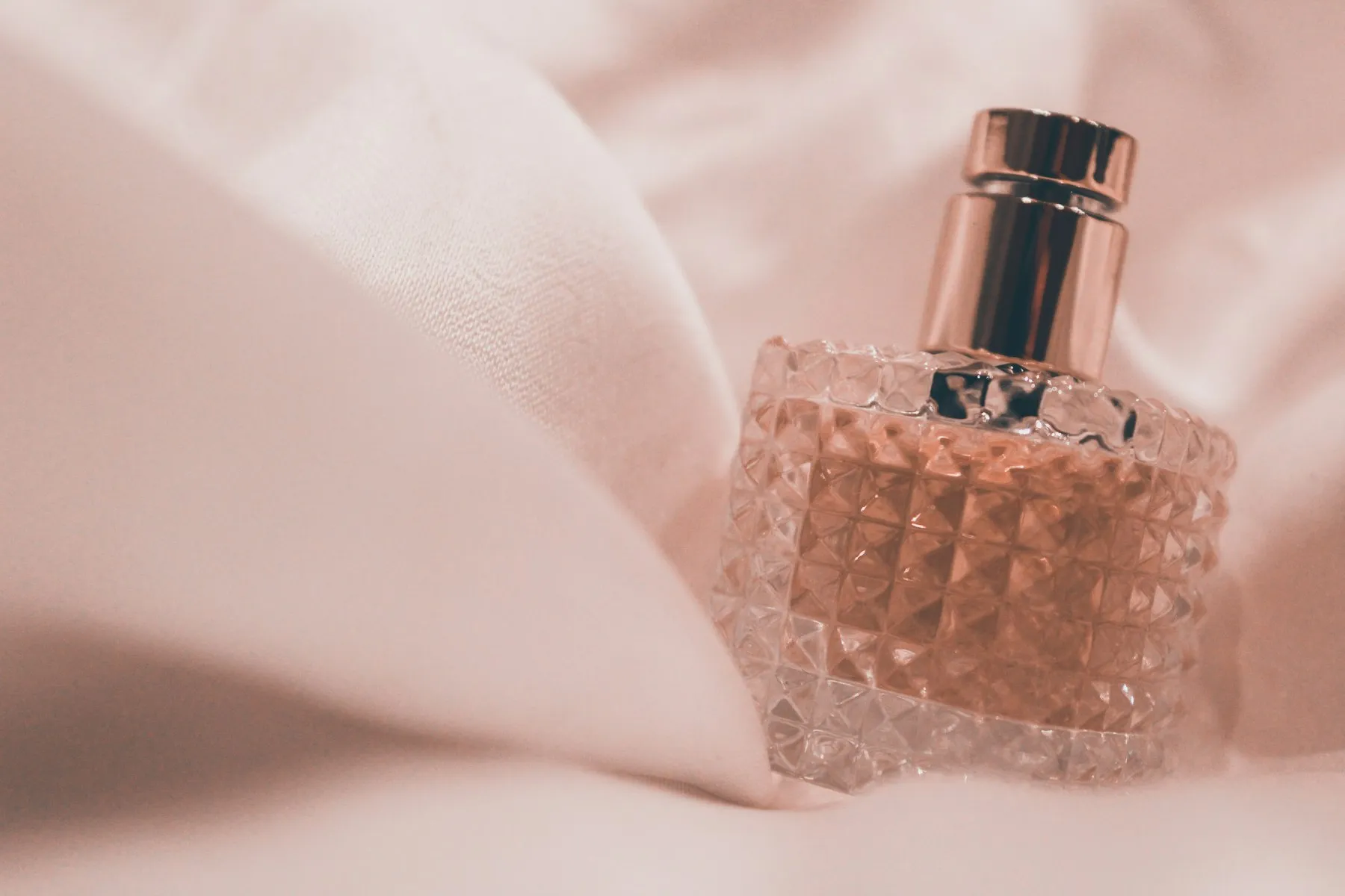 A pink cut-glass perfume bottle resting on soft pink fabric