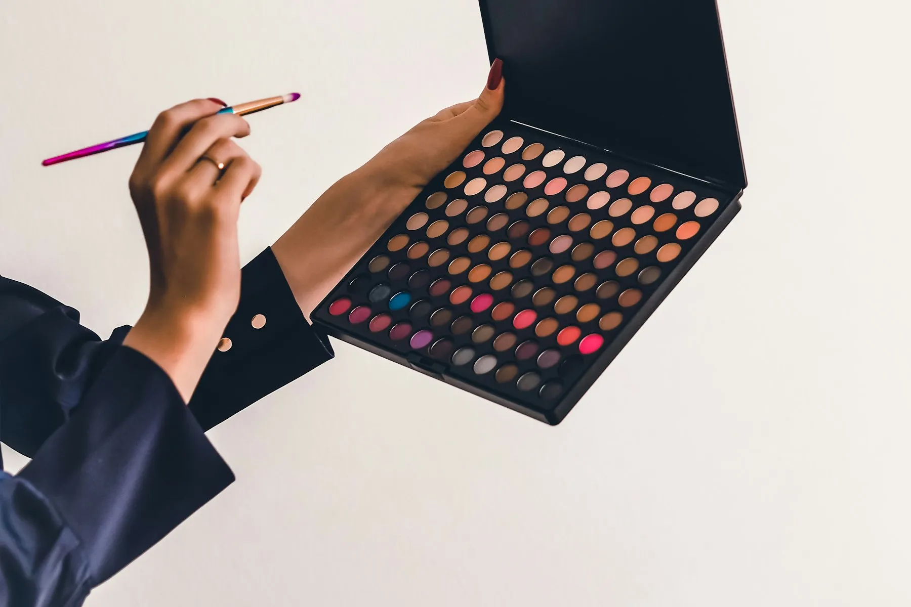 A person holding a large multi-shade eyeshadow palette and a brush