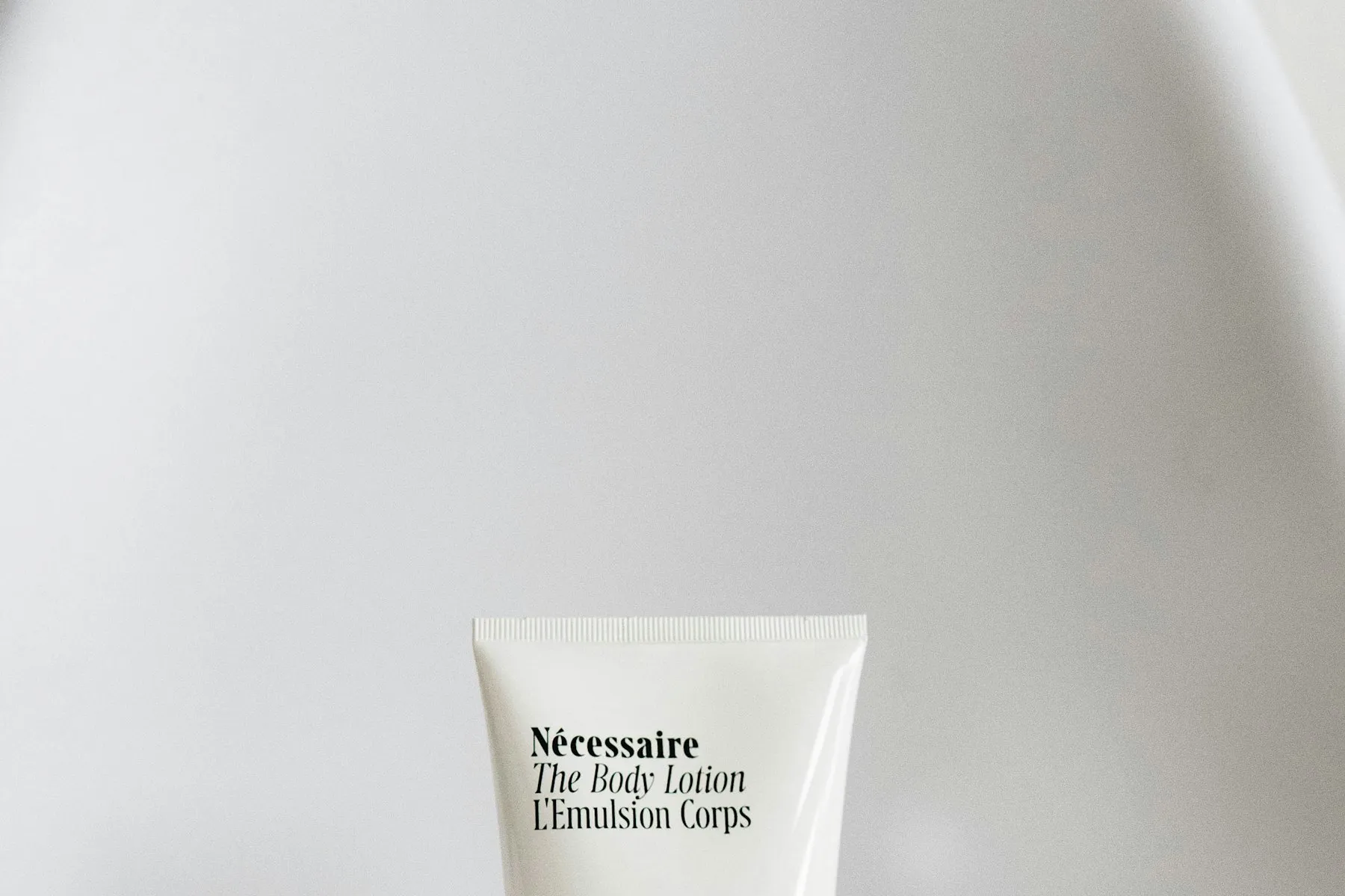 A white body lotion tube resting on soft crumpled fabric