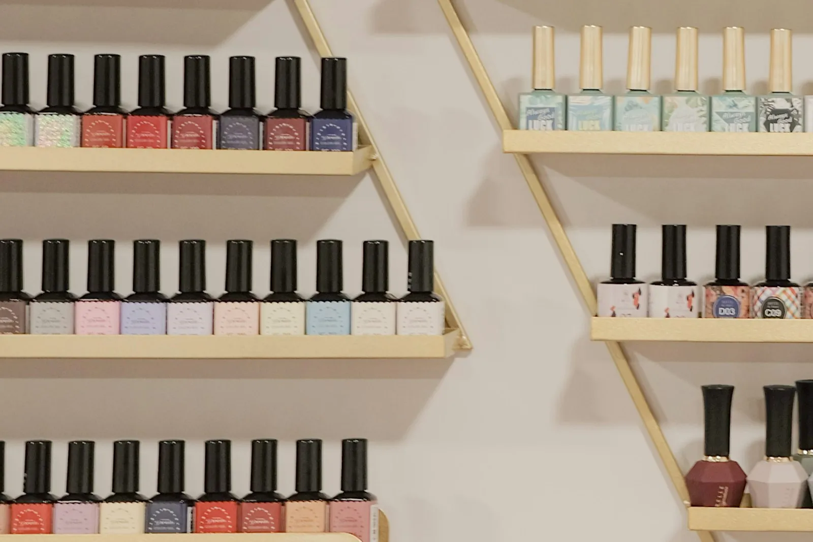 Rows of nail polish bottles on gold triangular wall shelves