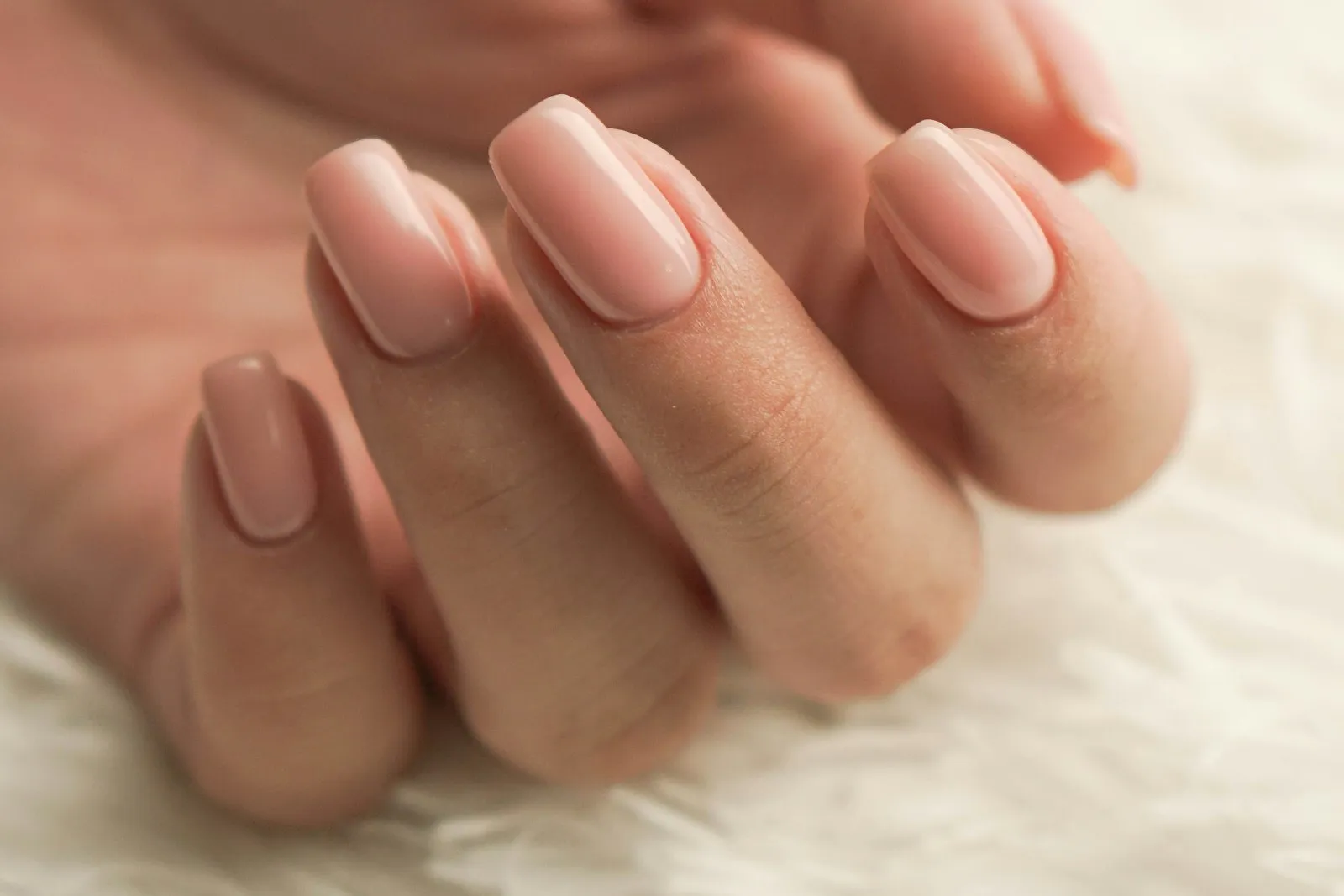 A hand with pale pink manicured nails resting on white fabric