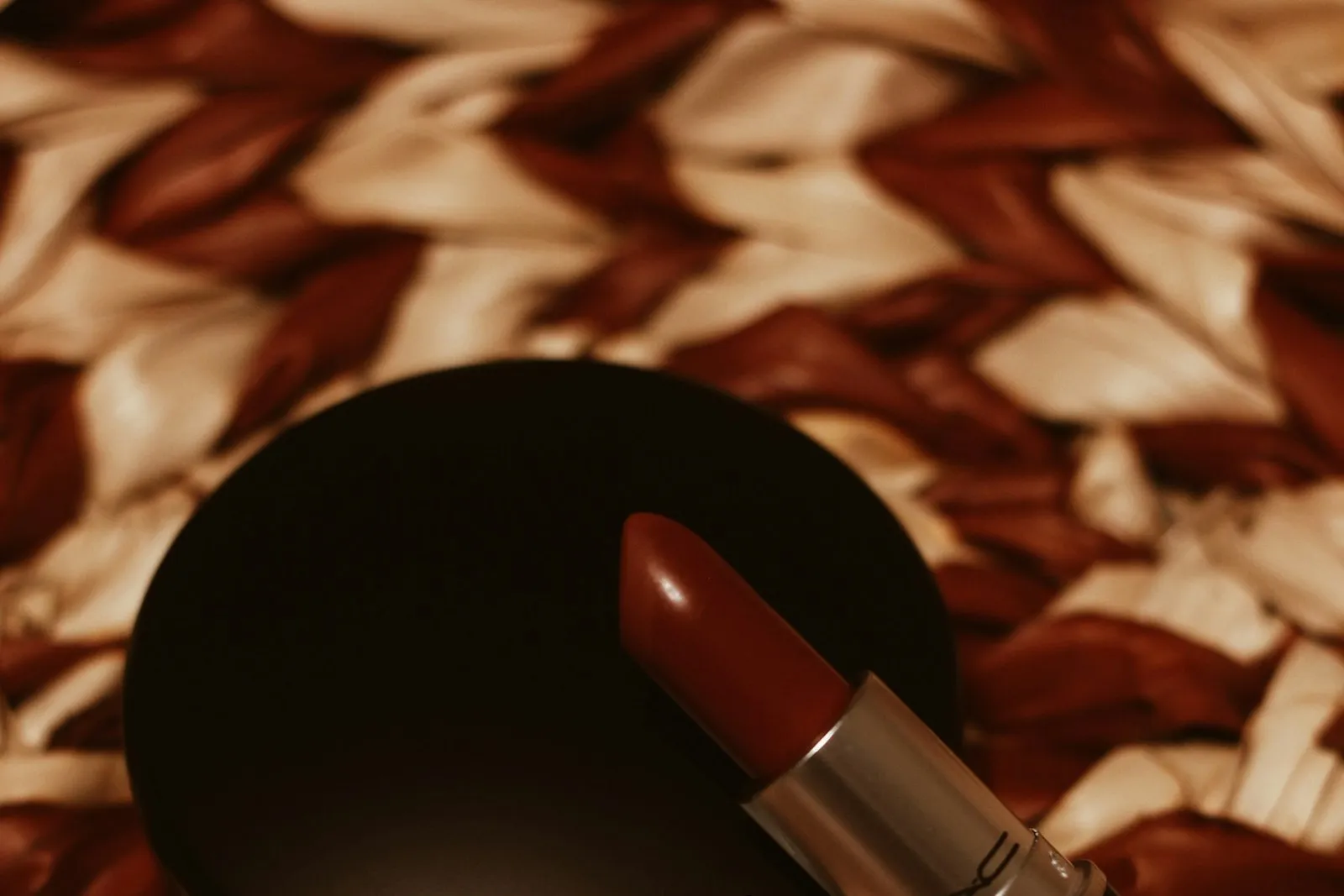 A red lipstick lying on brown and white woven fabric