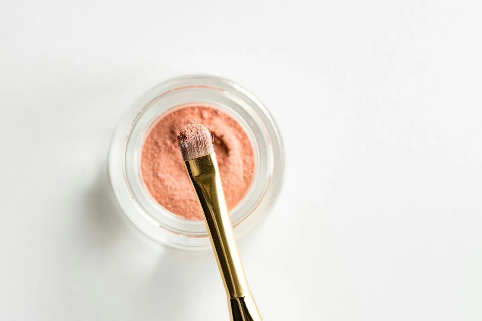 A makeup brush loaded with pink powder resting on a glass case